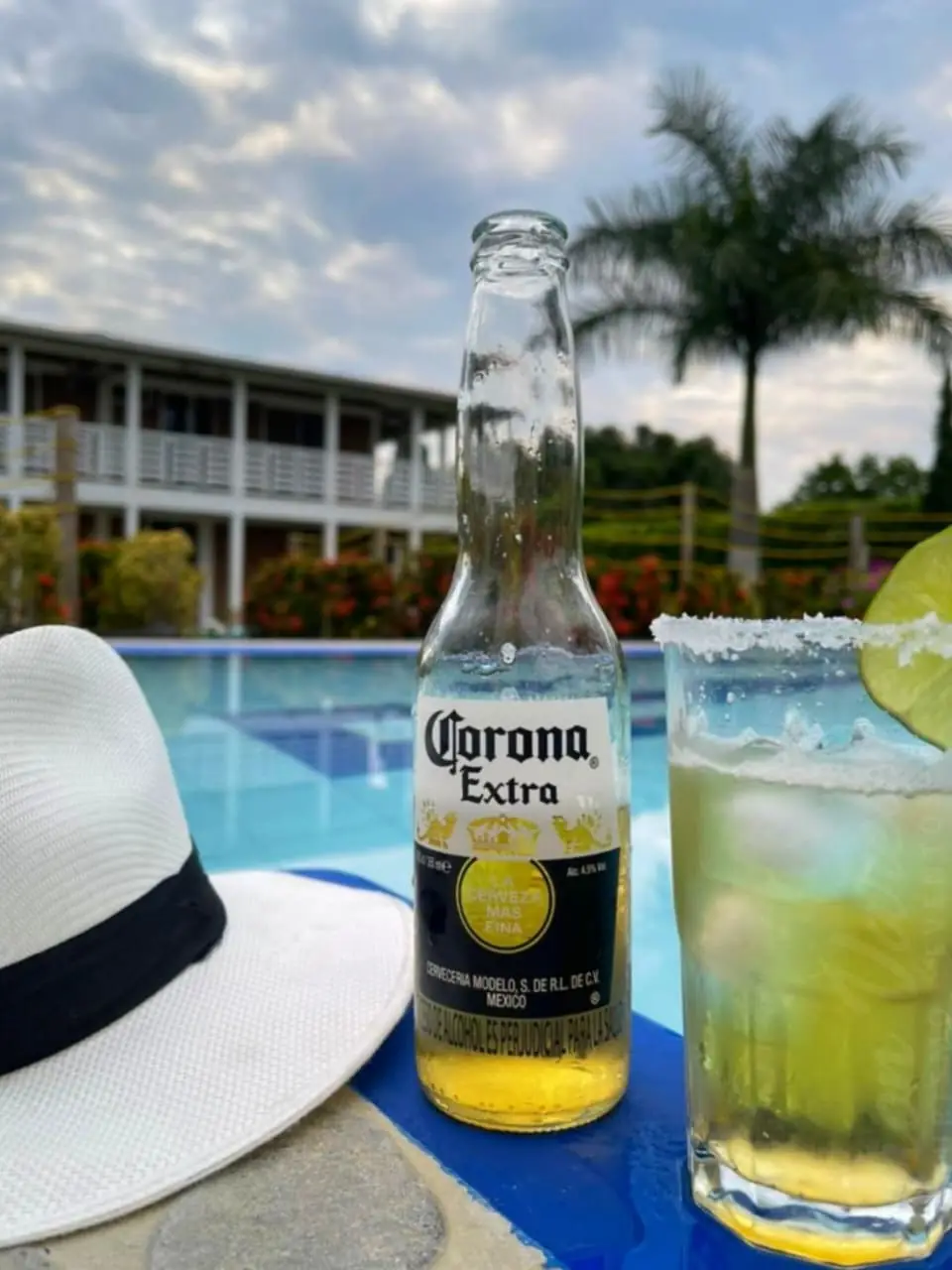Sombrero, cerveza y coctel de limón al borde de la piscina de una finca